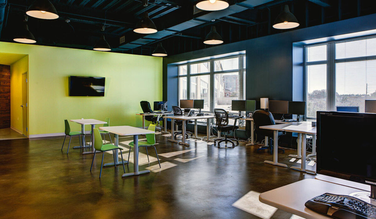 Open work area with desks and monitors by large windows and green café-style seating