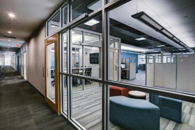 Glass-front meeting rooms and blue lounge seating beside open workstations, Orlando office