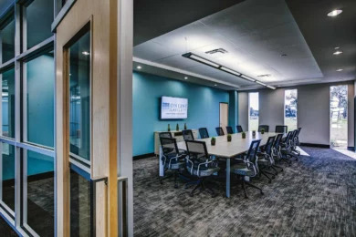 Conference room with long table, mesh-back ergonomic chairs, and wall-mounted display on teal wall