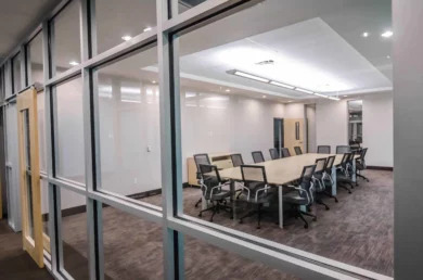 Glass-walled conference room with wood-framed door and mesh-back chairs around a long table