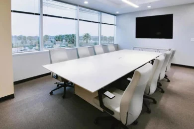 Conference room with white table, white ergonomic chairs, and wall-mounted display by large windows
