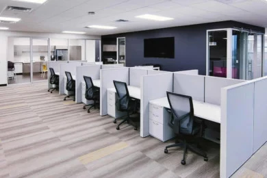 Row of low-panel workstations with ergonomic chairs and a glass-front room beyond