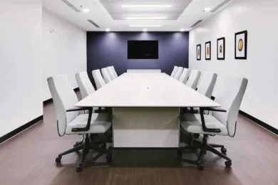 Long white conference table with white chairs and navy accent wall with wall-mounted display