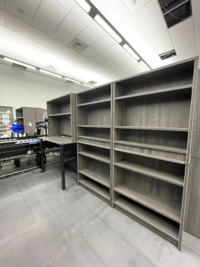 Gray woodgrain open bookcases beside a tall work table with monitor arm, Central Florida