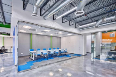 Glass-front conference room with blue chairs in an open office with exposed ceiling, Orlando