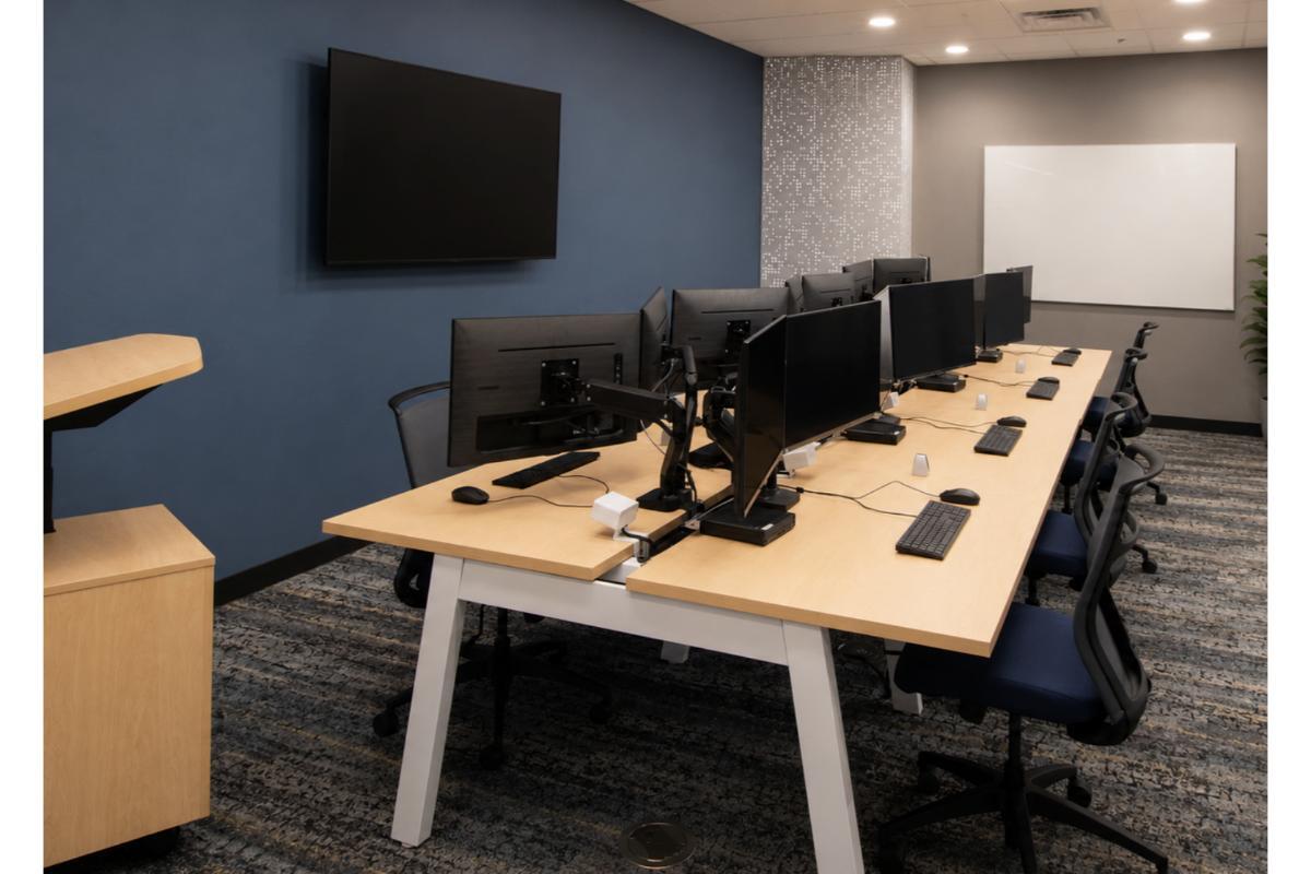 Computer lab with light wood bench desks, monitor arms, and mesh task chairs, Orlando university project