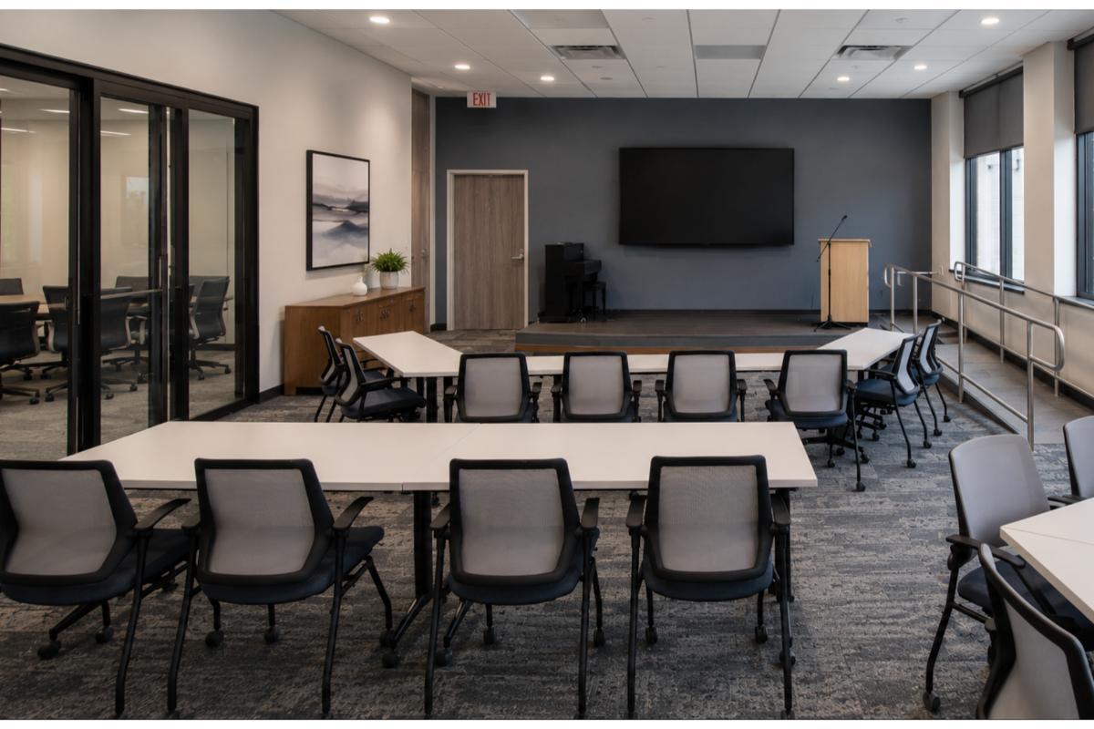 Multipurpose room with white training tables, mesh chairs, podium, and wall-mounted display