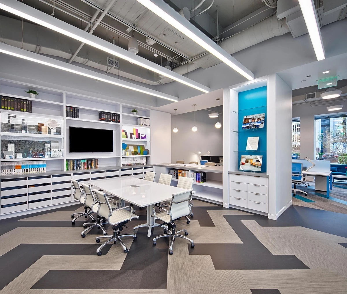 Architectural firm conference area with white storage drawers, glass display niche, and open workstations in the background