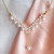 collier avec chaîne plaquée or et pendentif en forme de V orné de perles blanches d'eau douce, montrant la variété de tailles de perles utilisées pour créer le motif, détail du pendentif suspendu, montrant la perle unique en son centre.
