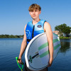 Man wearing the O'Brien Men's Flex V-Back LTD Life Jacket in blue, standing by a lake holding a wakesurf board and tow rope. Man wearing the O'Brien Men's Flex V-Back LTD Life Jacket in blue, standing by a lake holding a wakesurf board and tow rope.