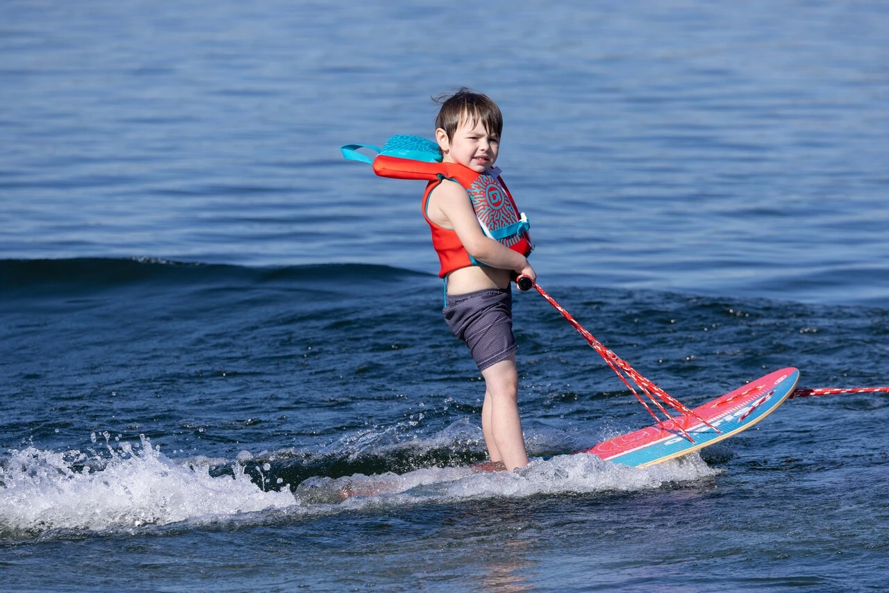 Child learning to waterski using O'Brien platform trainer on calm lake