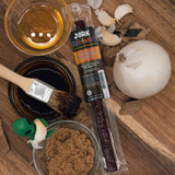 Honey BBQ beef stick package surrounded by raw ingredients and a basting brush from Uranus Fudge Factory.