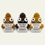 Three crocheted Emotional Support Poop stuffies in light brown, dark brown, and yellow holding Uranus Fudge Factory signs