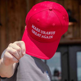 Hand holding up the red Make Uranus Great Again hat, white embroidered lettering facing forward.