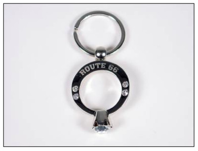 A silver metal souvenir keychain shaped like a diamond engagement ring with Route 66 text and rhinestones