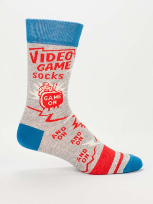 A single light heather grey crew sock displayed against a plain white background. The sock features bright blue accents on the top cuff, heel, and toe, along with a wide red stripe near the toe. Knit into the ankle, framed by jagged red zigzag lines, is the bold red text: "VIDEO GAME socks". Below it is a retro line-art illustration of a person sitting closely in front of a glowing red tube TV; the TV screen reads "GAME ON". Continuing down the foot of the sock, red text repeats the phrase "AND ON" three separate times.