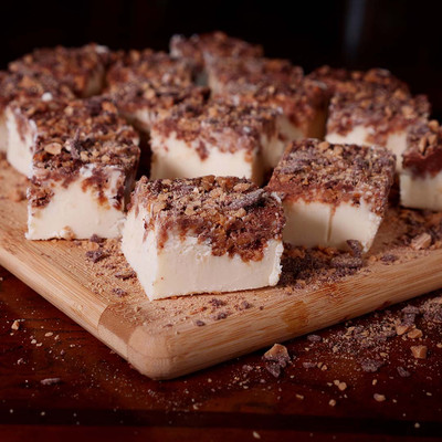 English toffee fudge squares covered in crushed candy on a wooden board by Uranus Fudge Factory.