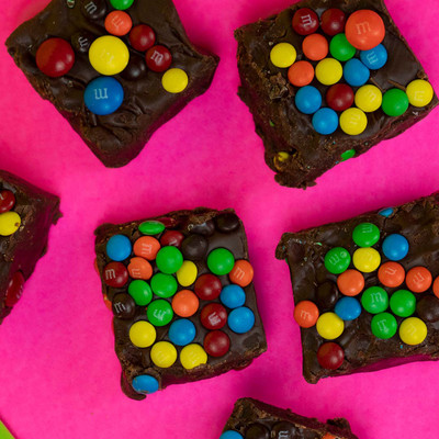Chocolate fudge with M&Ms on pink poster board.