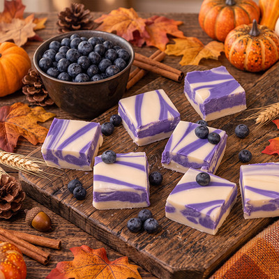 Purple and vanilla blueberry swirl fudge squares with a bowl of blueberries and autumn decor on a rustic table