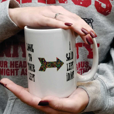 Person holding a white coffee mug with a funny arrow graphic and a sarcastic left quote.