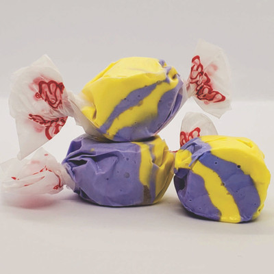 Three colorful wrapped Raspberry Lemonade saltwater taffy candies stacked together on a plain white background by Uranus Fudge Factory.