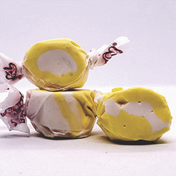 Three colorful wrapped buttered popcorn saltwater taffy candies stacked together on a plain white background by Uranus Fudge Factory.
