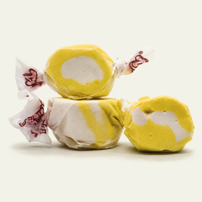 Three colorful wrapped buttered popcorn saltwater taffy candies stacked together on a plain white background by Uranus Fudge Factory.
