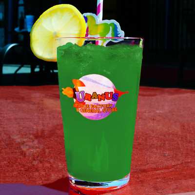 Green drink in a custom logo pint glass on a table with a dark blurred outdoor background at Uranus Fudge Factory.