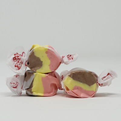 Three pieces of brown, yellow, pink salt water taffy candies wrapped in wax paper.