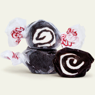 Three pieces of black salt water taffy candies with white details wrapped in wax paper.