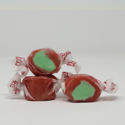 Three pieces of red salt water taffy candies with green centers wrapped in wax paper.