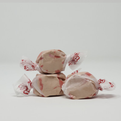 Three pieces of tan salt water taffy candies with red stripes wrapped in wax paper.