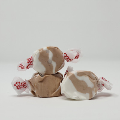 Three pieces of brown and white salt water taffy candies wrapped in wax paper.