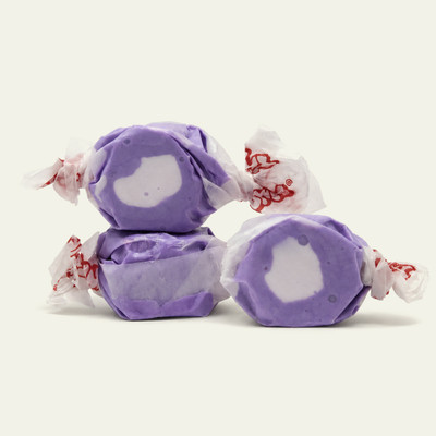 Three pieces of purple salt water taffy candies with white centers wrapped in wax paper.