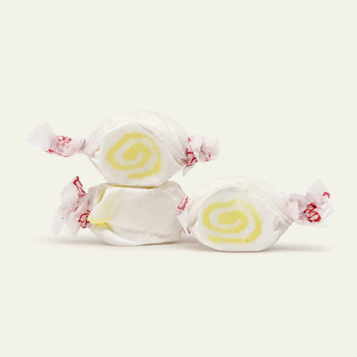 Three pieces of white salt water taffy candies with yellow swirls wrapped in wax paper.