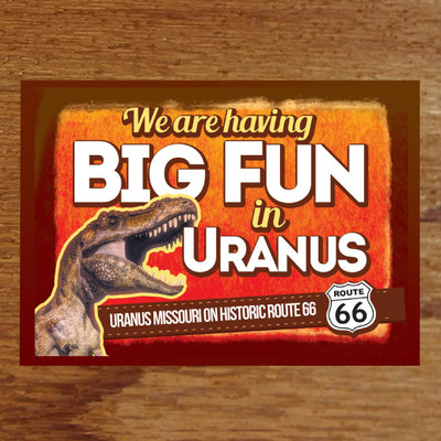 A horizontal postcard featuring a roaring T-Rex next to the large, bold text "We are having BIG FUN in URANUS" set against a textured orange background. A brown banner across the bottom reads "URANUS MISSOURI ON HISTORIC ROUTE 66" alongside a classic black and white Route 66 highway shield.