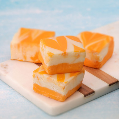 Uranus Orange Cream Fudge is a perfect summer confection. Displayed on a white and brown cutting board with sky blue background.