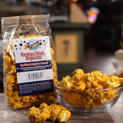 Uranus Style Popcorn bag next to a glass bowl with a blurred store background by Uranus Fudge Factory.