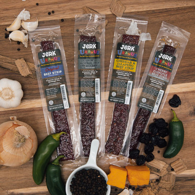 Four flavors of packaged Jerk Uranus beef strips displayed on a wooden board from Uranus Fudge Factory.