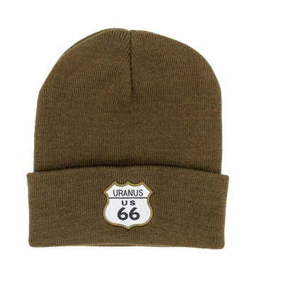 A dark olive green knit cuffed beanie hat against a plain white background. The front cuff features a sewn-on white patch shaped like a classic highway shield with an olive green border.
