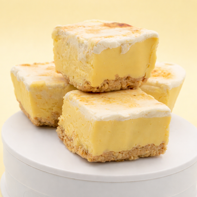 Uranus Lemon Meringue Pie Fudge with toasted topping displayed in a stack of four on a white platform. The background is pale yellow like a sunrise.