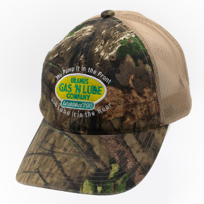 Angled side view of green camo Gas N Lube trucker hat showing curved brim, mesh back, and embroidered front patch.