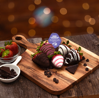Chocolate-dipped strawberries displayed on a wooden serving board, decorated with dark, milk, and white chocolate drizzles, with fresh berries and chocolate pieces around them.