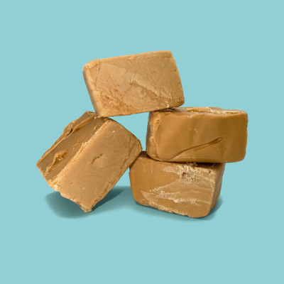 Four pieces of penuche fudge stacked at angles on a teal background, showing the smooth, creamy texture and caramel-brown color.
