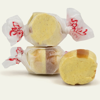 Three pieces of yellow salt water taffy candies with brown stripes wrapped in wax paper.