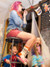 A pink-haired woman drinks wine on a stool wearing the "Shit Show" socks while kids play around her.
