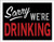 A humorous black sign featuring text that reads Sorry WE'RE DRINKING in white, gray, and red