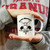 A person holding a white Uranus Mortuary novelty ceramic mug from Uranus Fudge Factory.