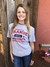 A smiling woman wearing a grey university t-shirt outdoors at Uranus Fudge Factory.
