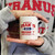 A person holding a white Uranus University ceramic mug from Uranus Fudge Factory.